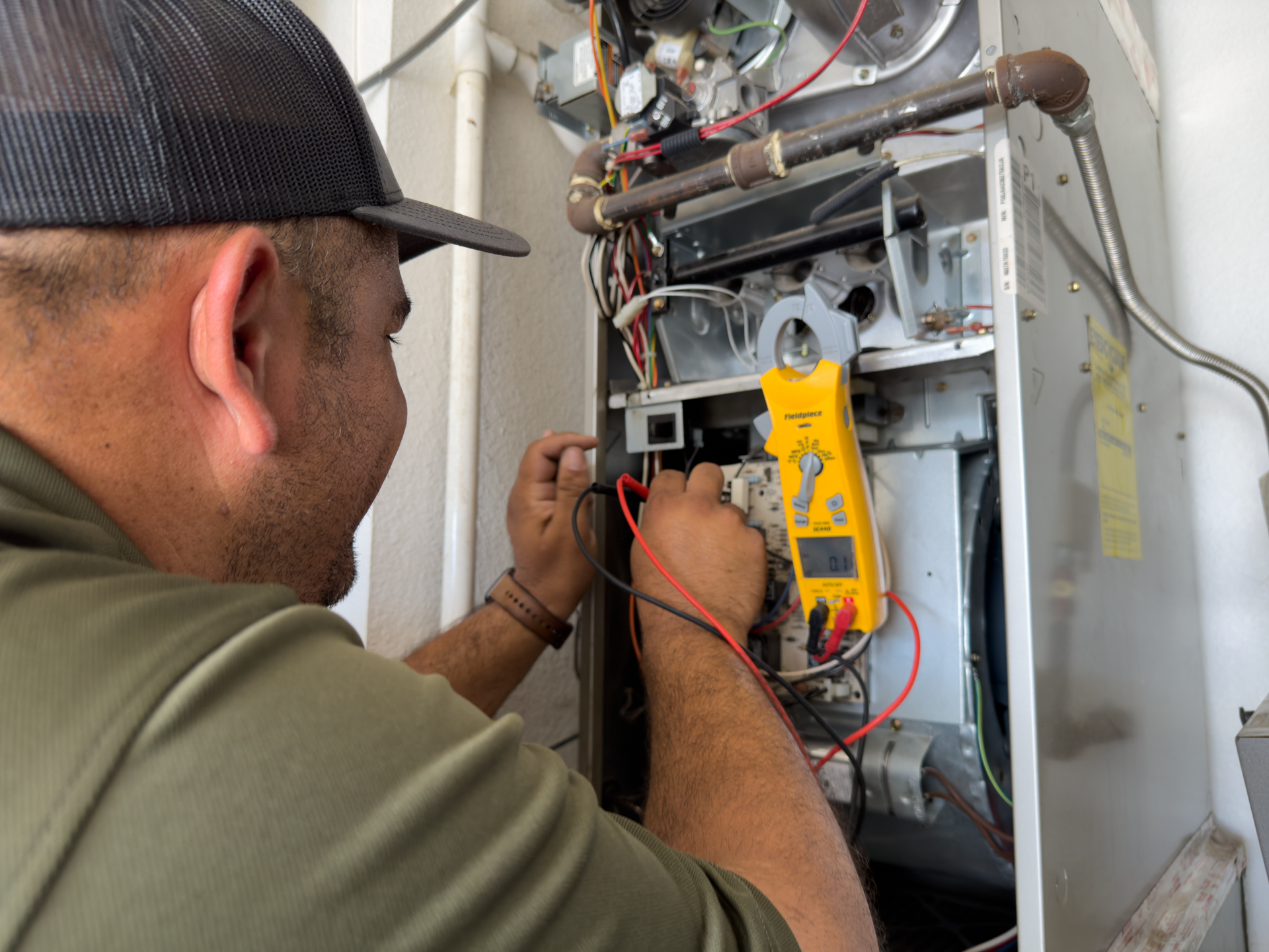 Technician inspecting wiring inside an open electrical panel with a yellow multimeter
