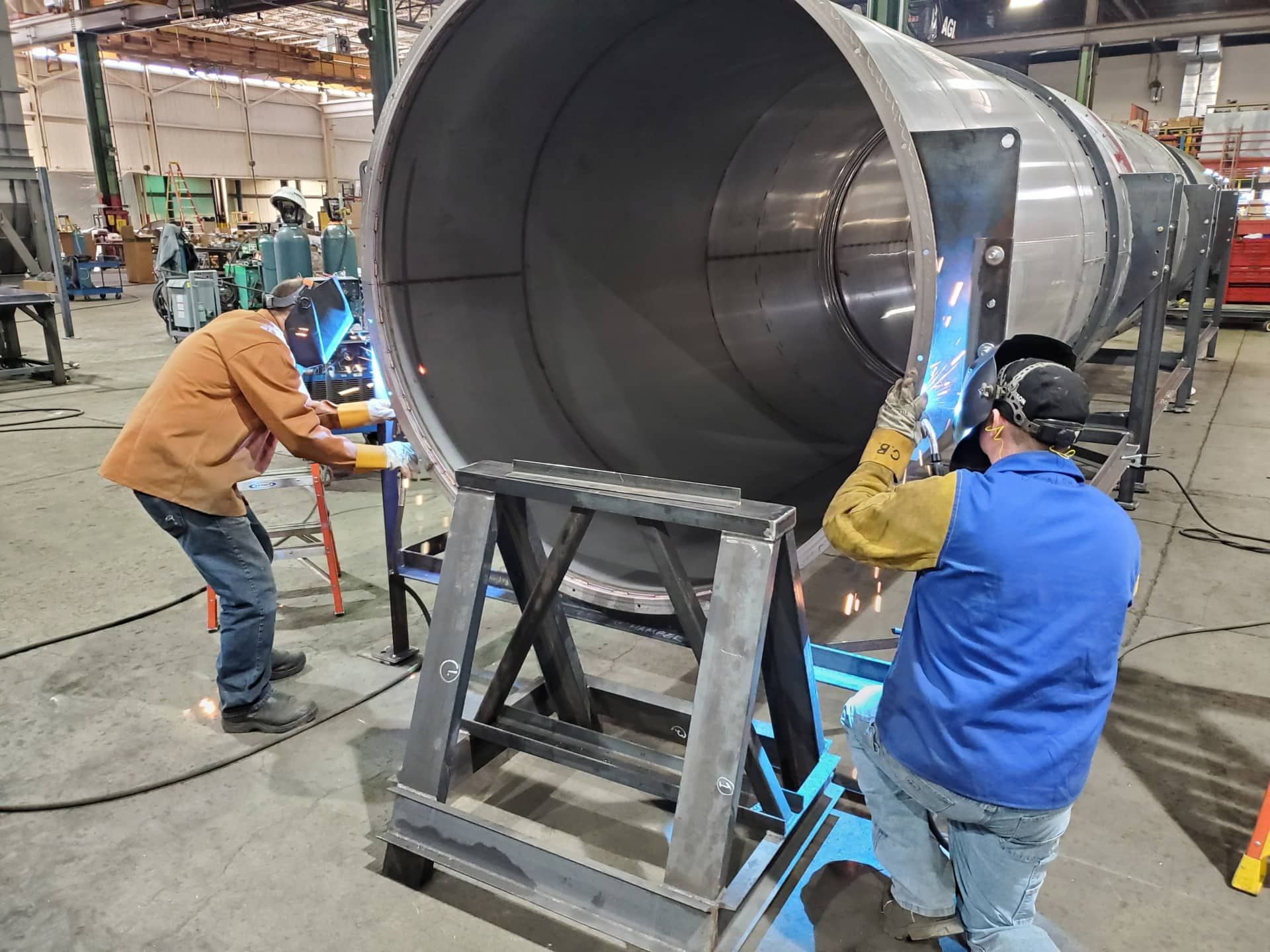 Workers assembling a large metal cylinder in a factory workshop