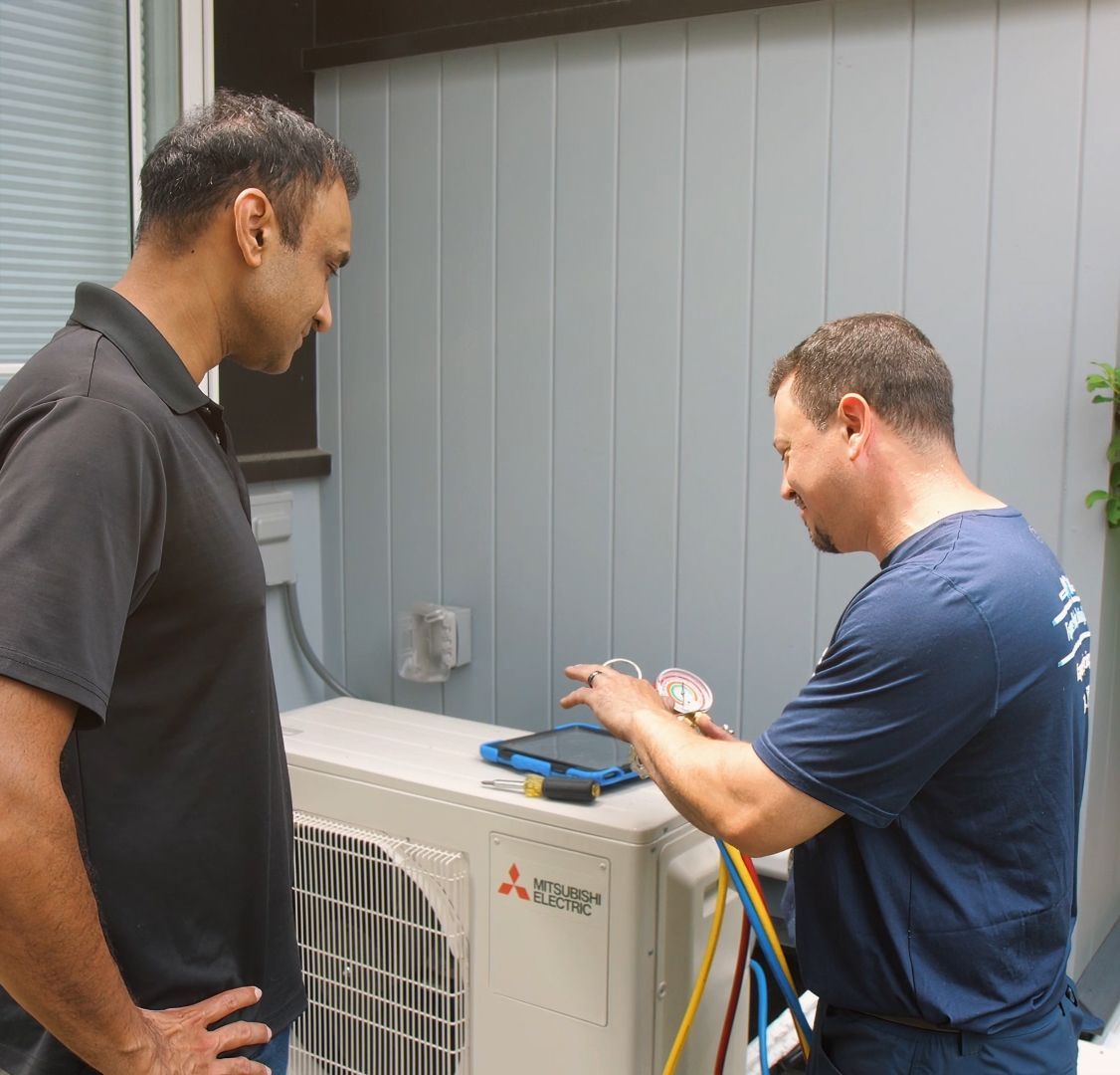 Two technicians inspect an outdoor Mitsubishi HVAC unit with tools and gauges.