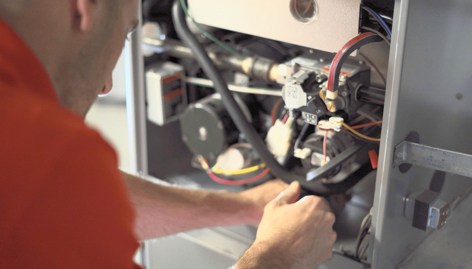 Technician in an orange shirt working on wiring inside an open machine panel.