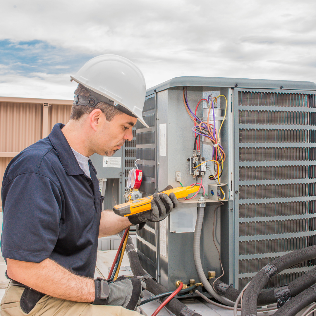 Technician in hard hat inspecting HVAC unit wiring with a multimeter outdoors