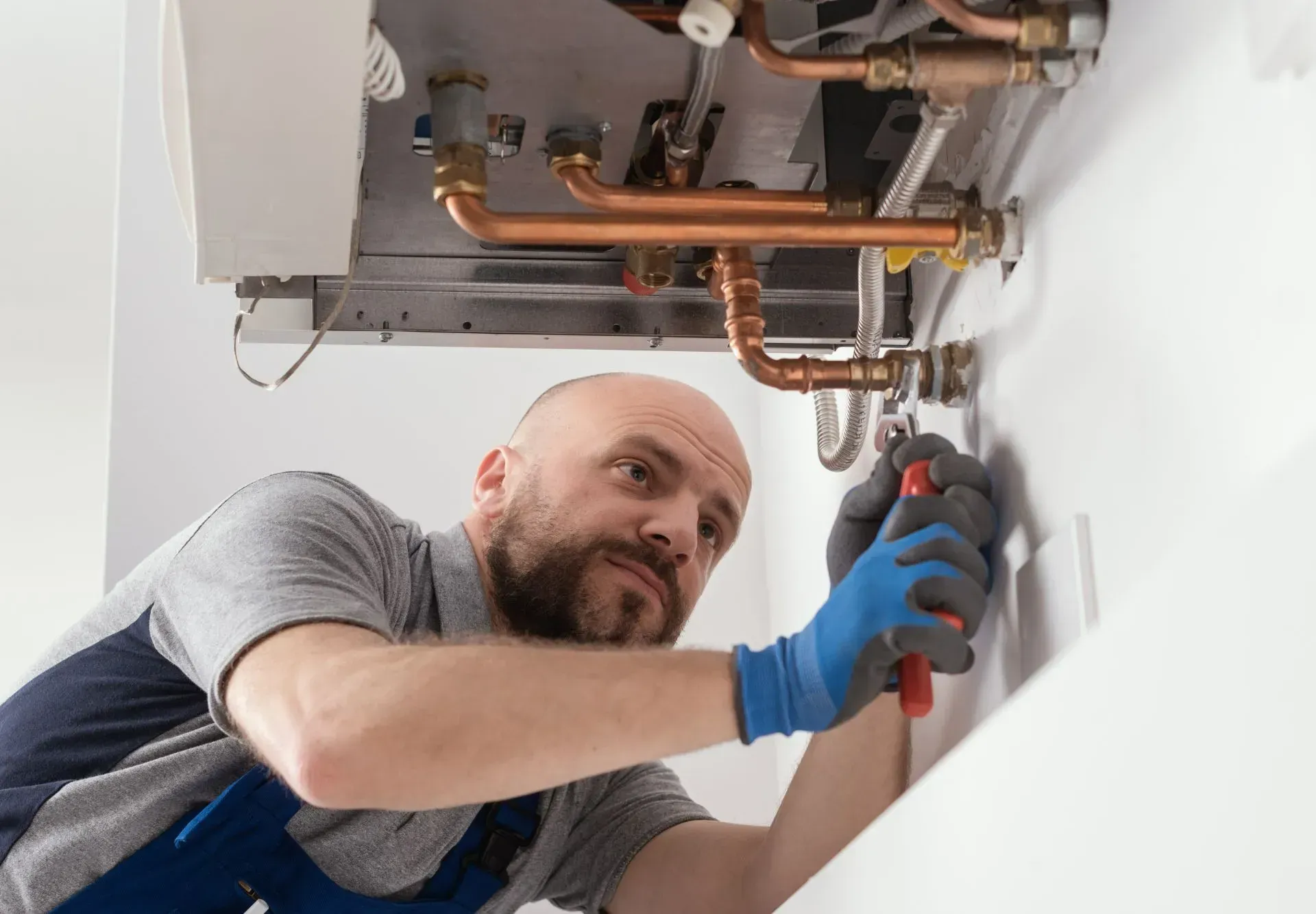 Technician in blue gloves repairing exposed copper pipes in a ceiling cavity