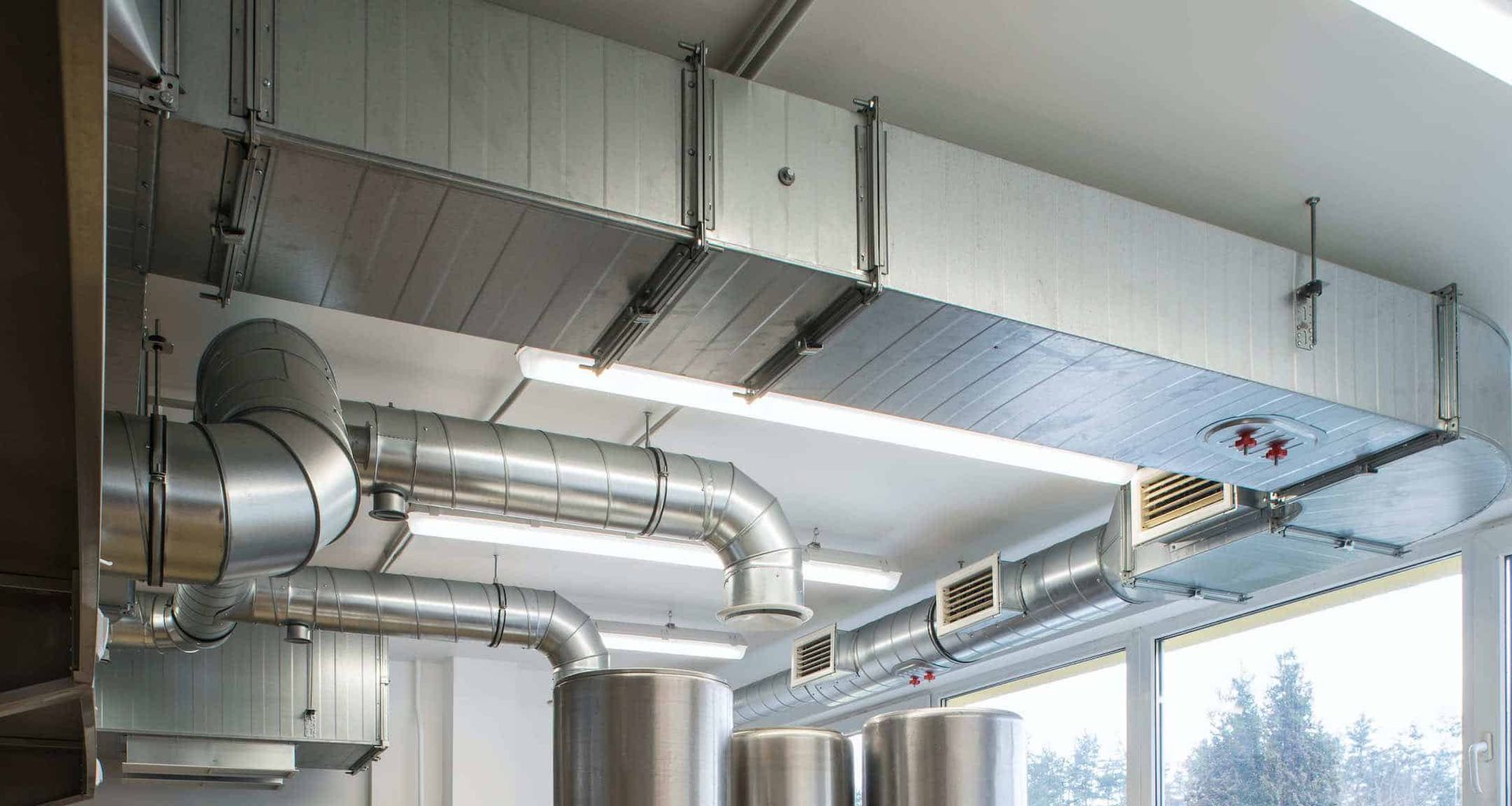 Industrial ceiling ductwork and vents in a bright mechanical room with windows below