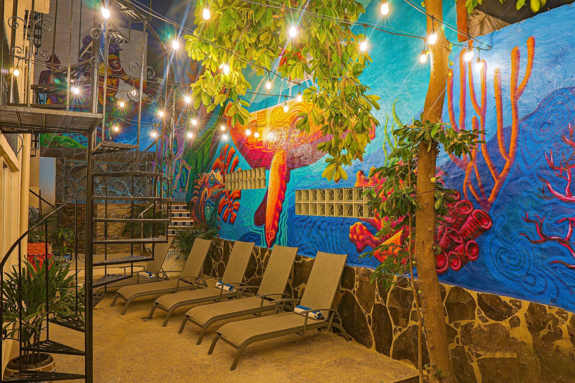 Patio with lounge chairs, mural of flamingo and coral reef, string lights.