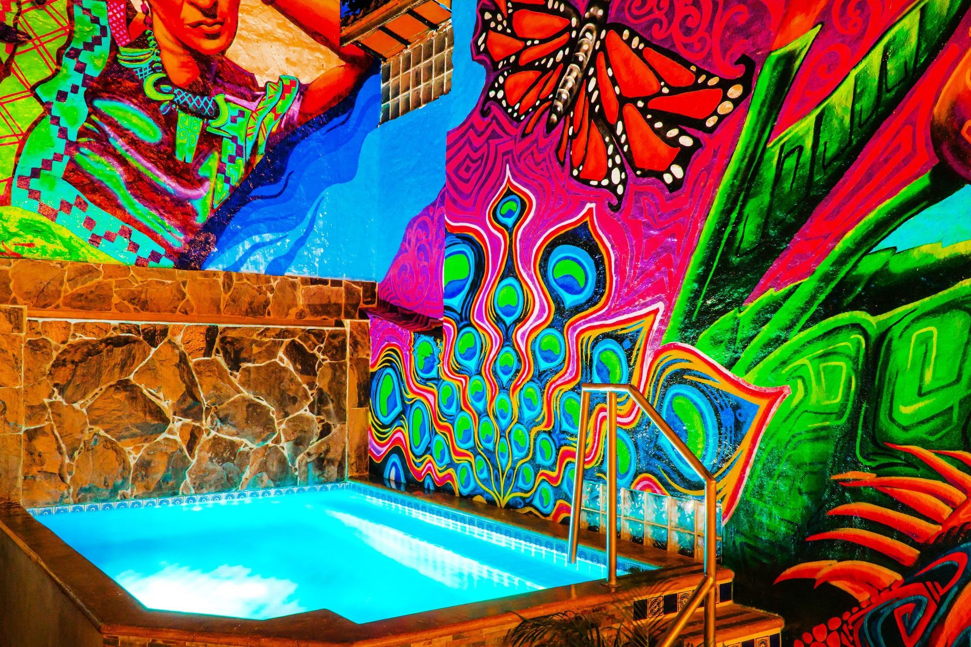 Pool with blue water, under colorful mural of butterfly, peacock feathers, and flowers.