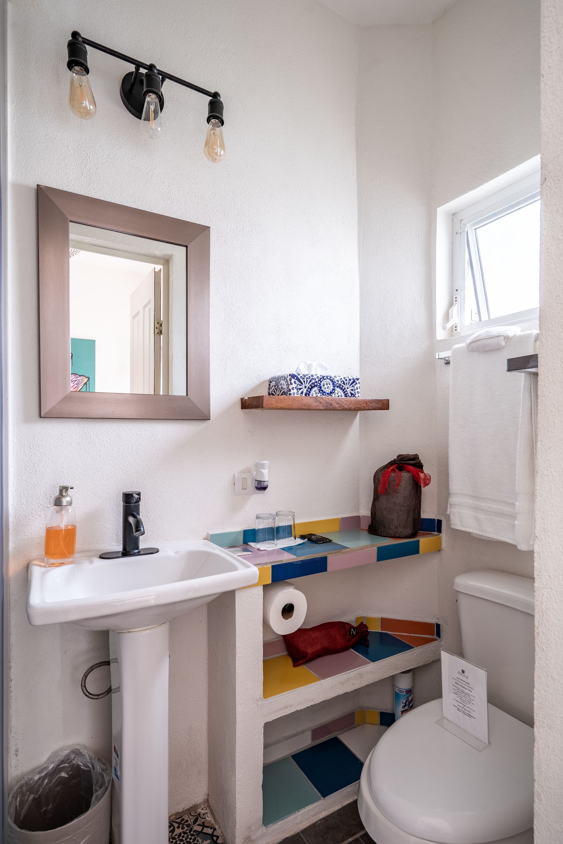Small bathroom with white sink, toilet, and colorful tiled counter.