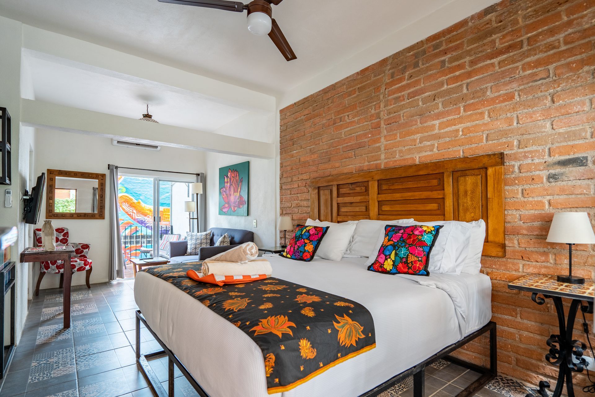Bedroom with exposed brick wall, king bed, colorful pillows, and balcony access.