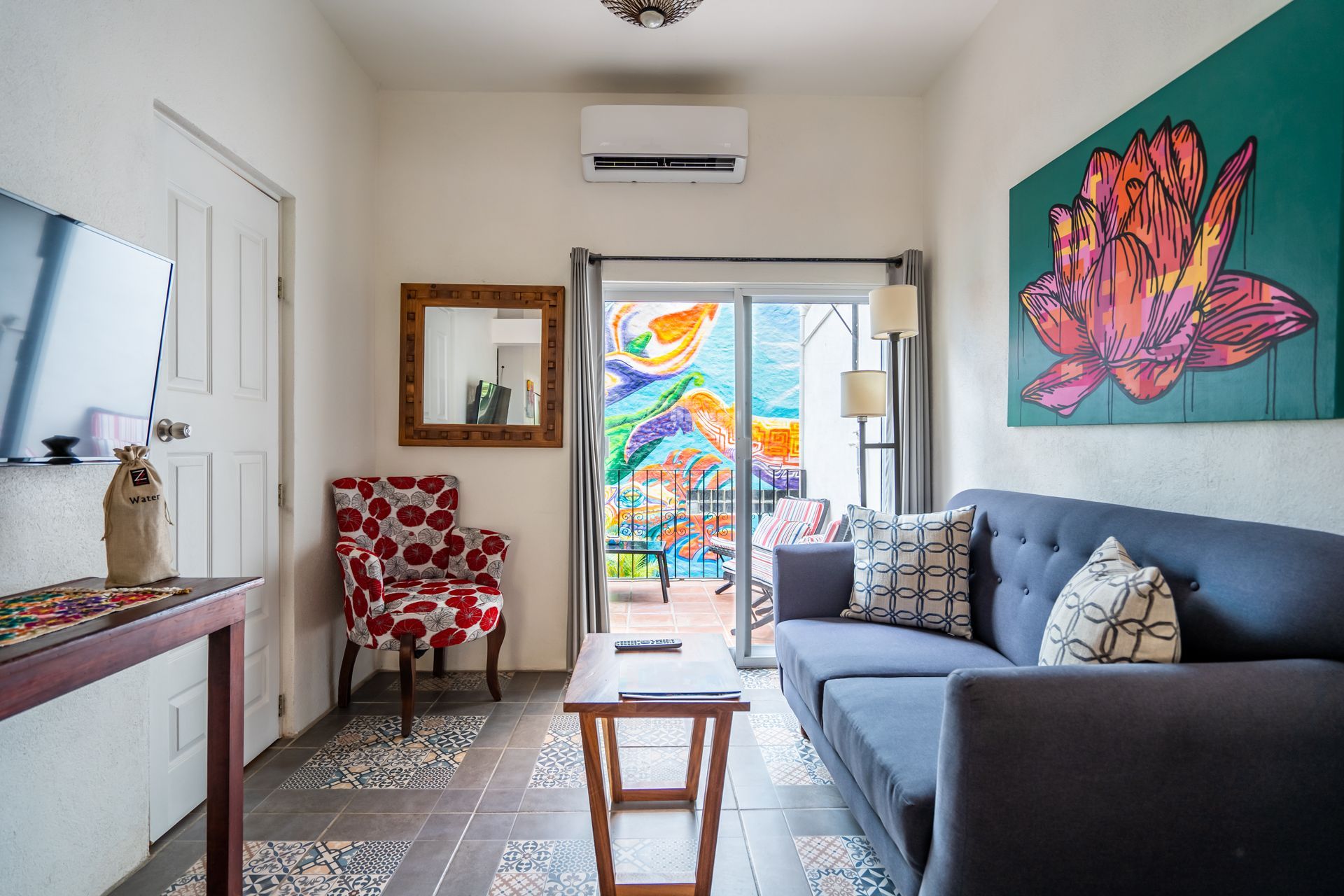 A cozy living room with a blue sofa, art, and a view of a colorful patio.