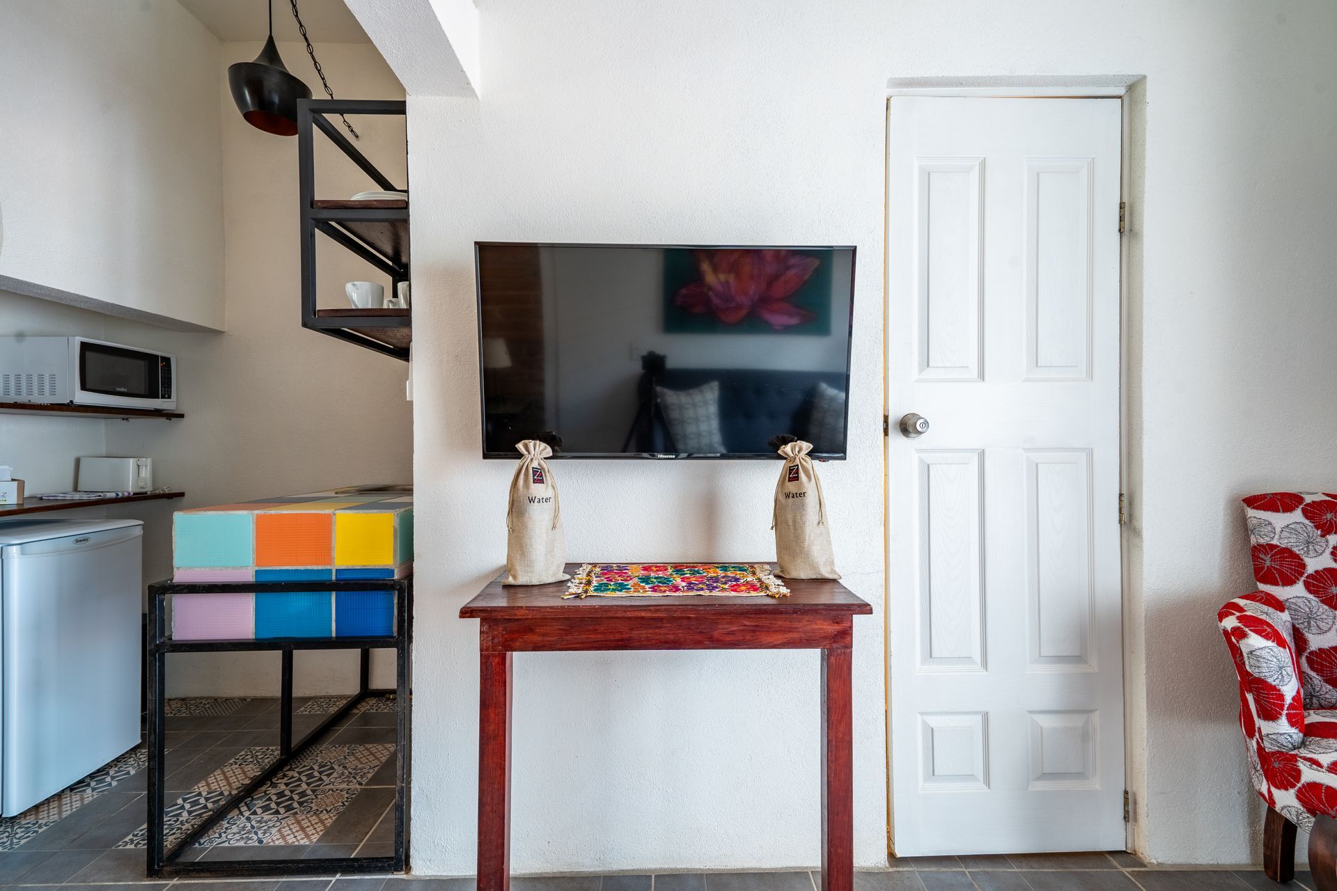 Cozy room with TV, door, and colorful cabinet, next to a small kitchen area and staircase.
