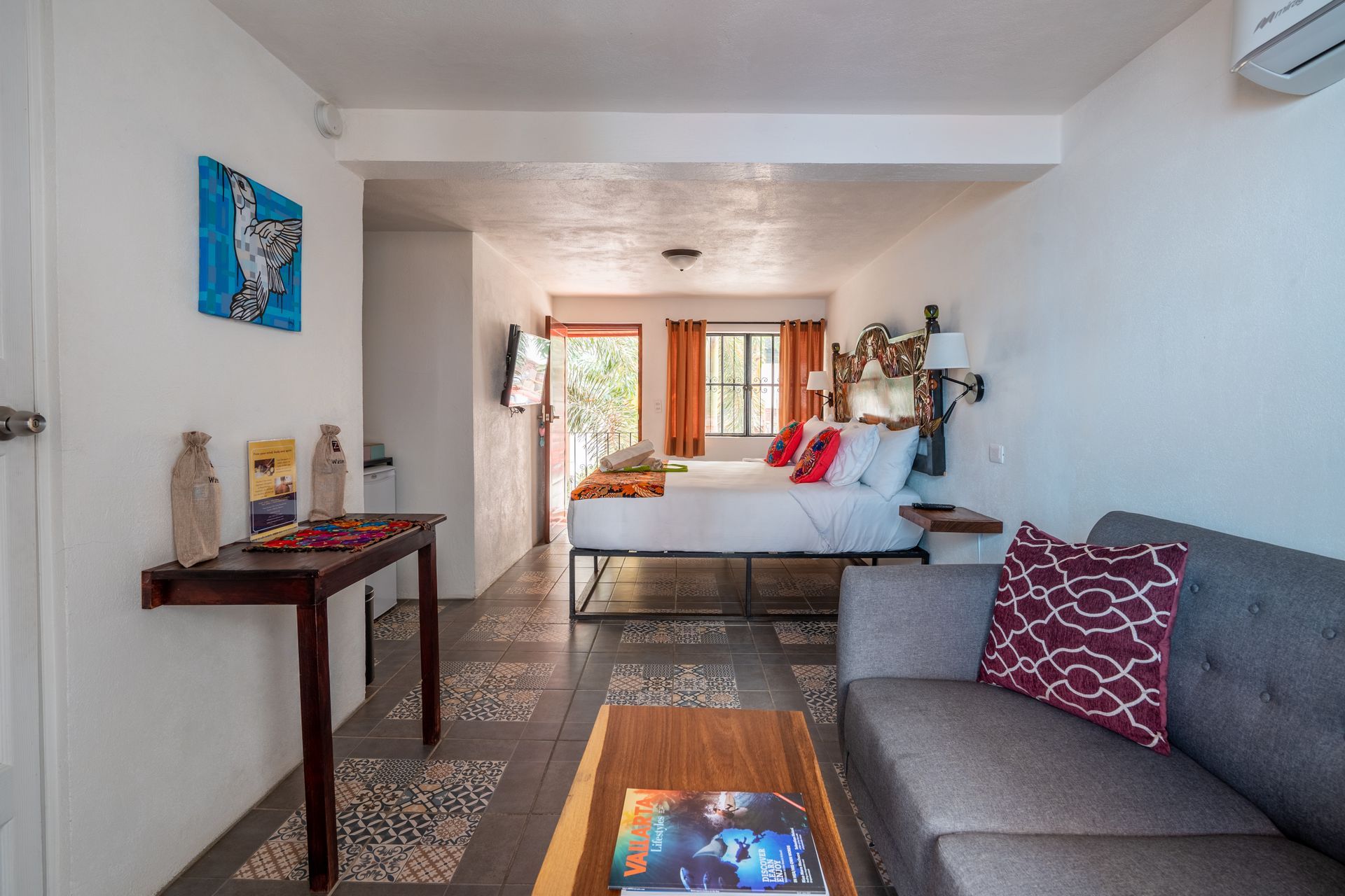 Bright hotel room with a bed, sofa, desk, and colorful art.
