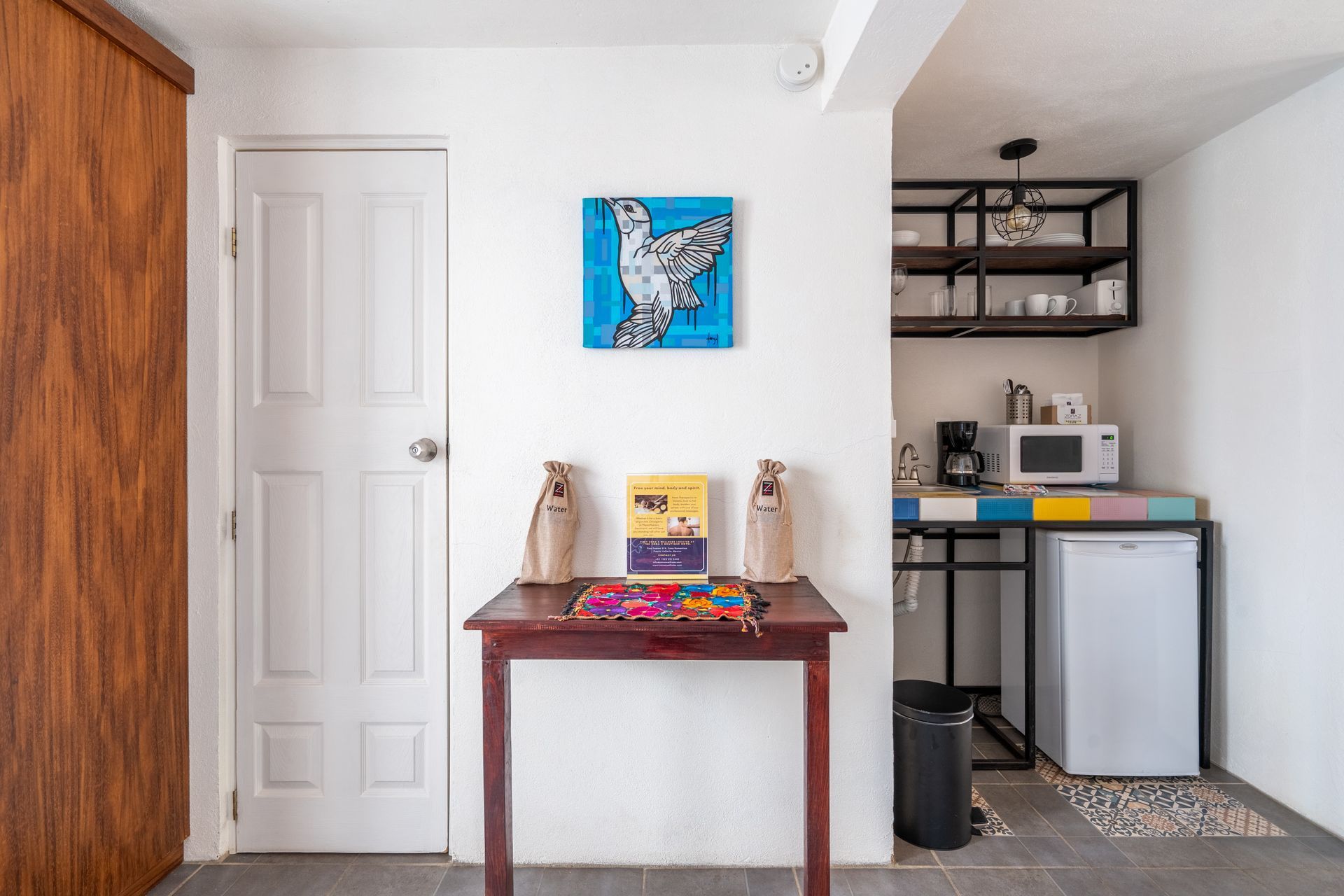 Small room with open kitchen area. Table with decorations, white door and painting.