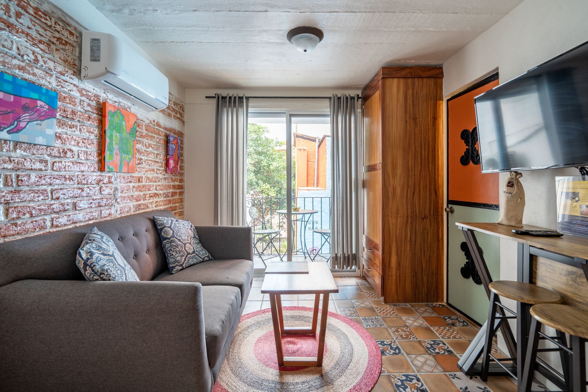 Living room with a gray sofa, brick wall with art, and a balcony.