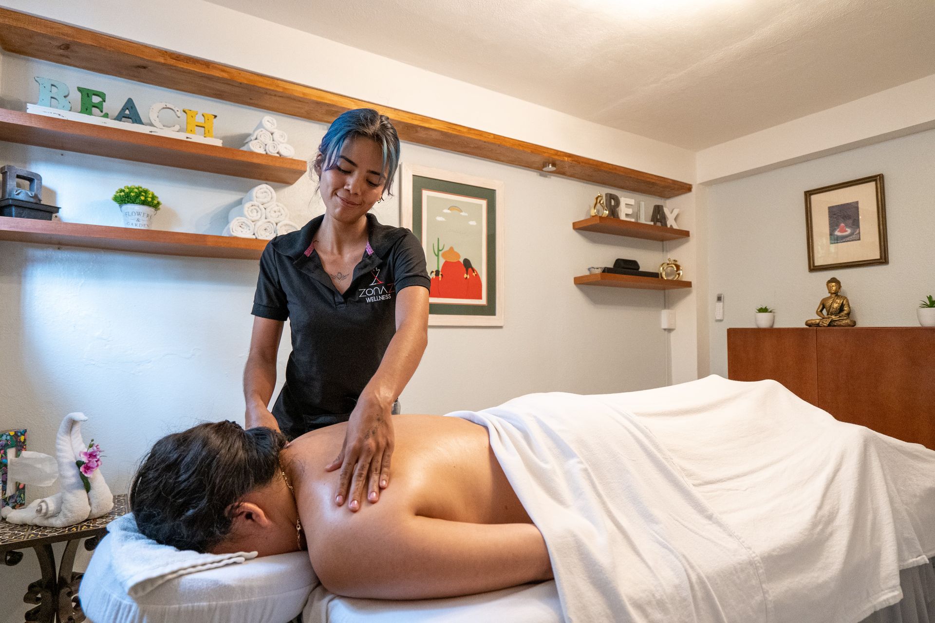 Massage therapist giving a back massage. Room with shelves, art, and a desk.