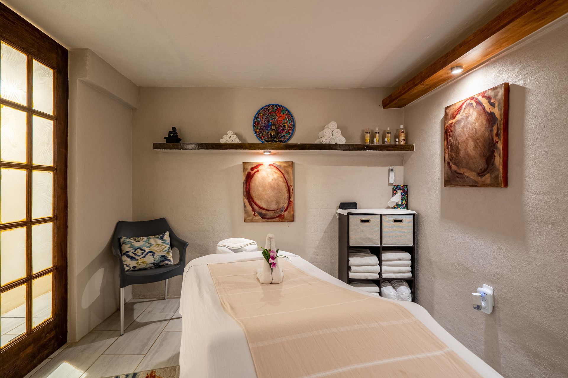 Massage room with massage table, art, shelves, and towels.