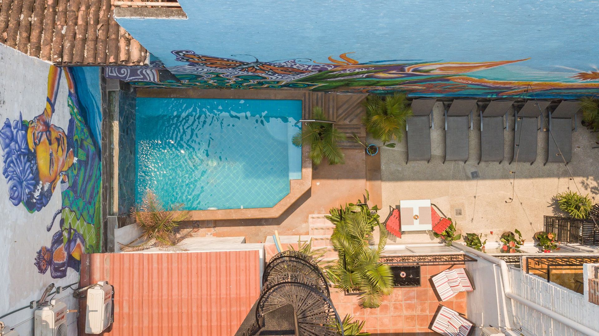 Overhead view of a courtyard with a pool, mural, lounge chairs, and a spiral staircase leading to a lower level.