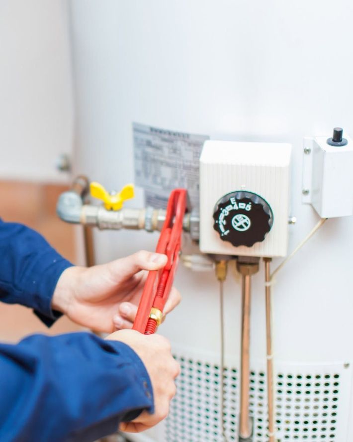 Person using red pliers to work on plumbing near a white water heater control panel.