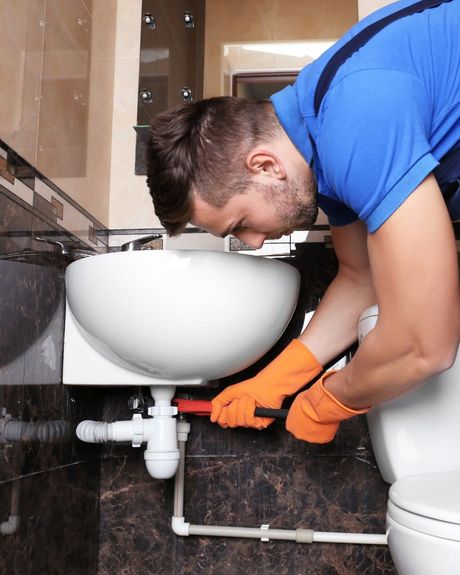 Plumber in orange gloves repairing sink plumbing with a wrench in a bathroom