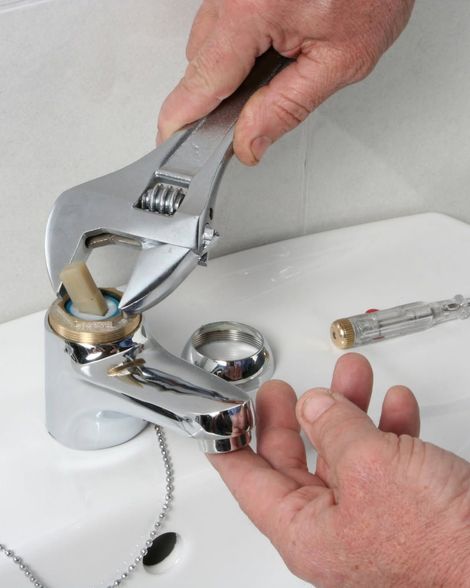 Hands using a wrench to adjust a bathroom sink faucet.