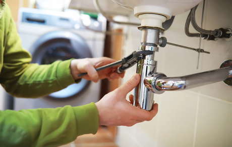 Person using pliers to repair a chrome sink drain under a bathroom sink