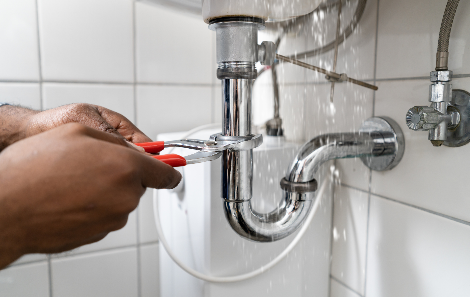 Hands using a red wrench to tighten a chrome sink pipe under a bathroom basin