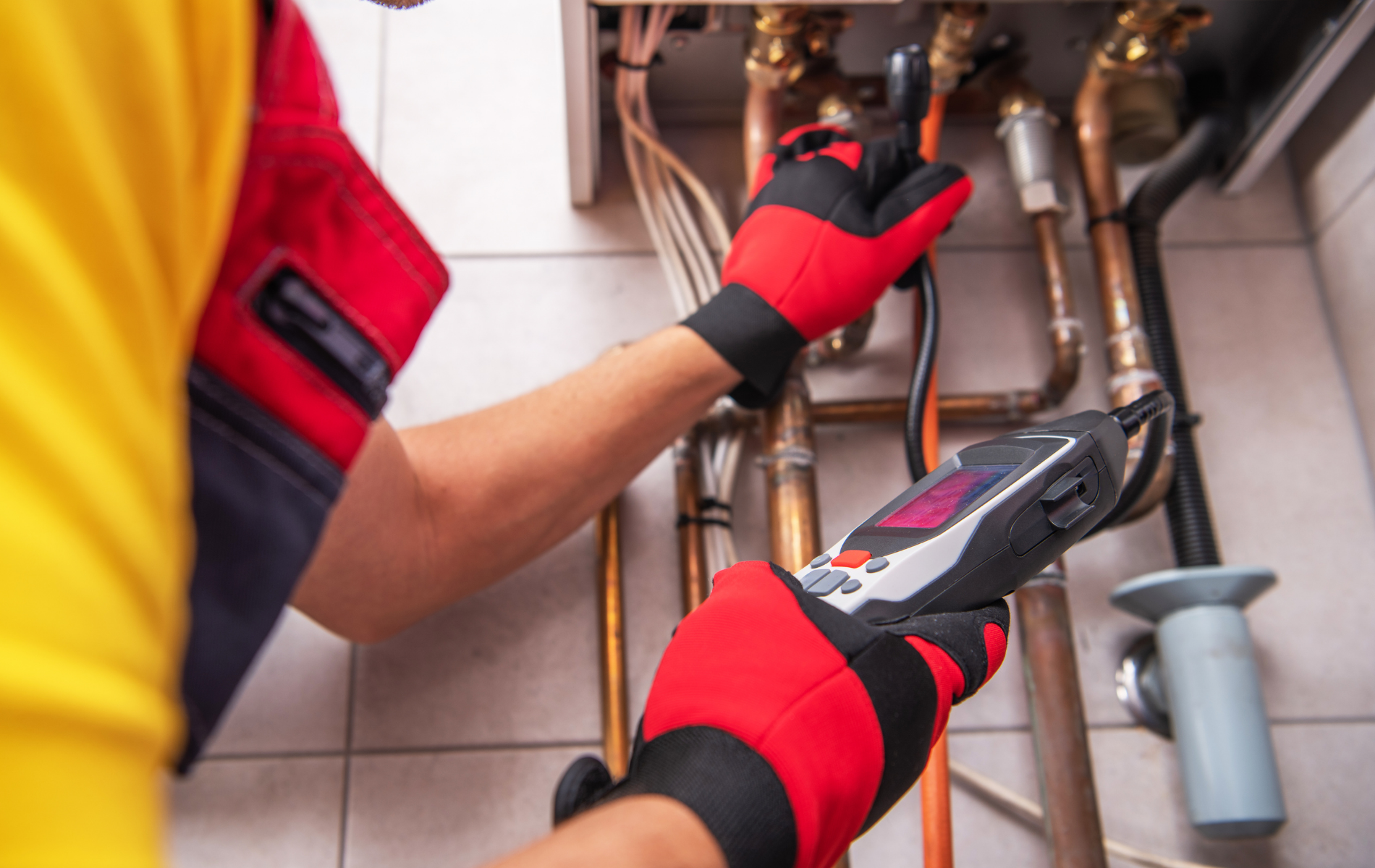 Technician with red gloves uses tools to inspect copper pipes under a sink