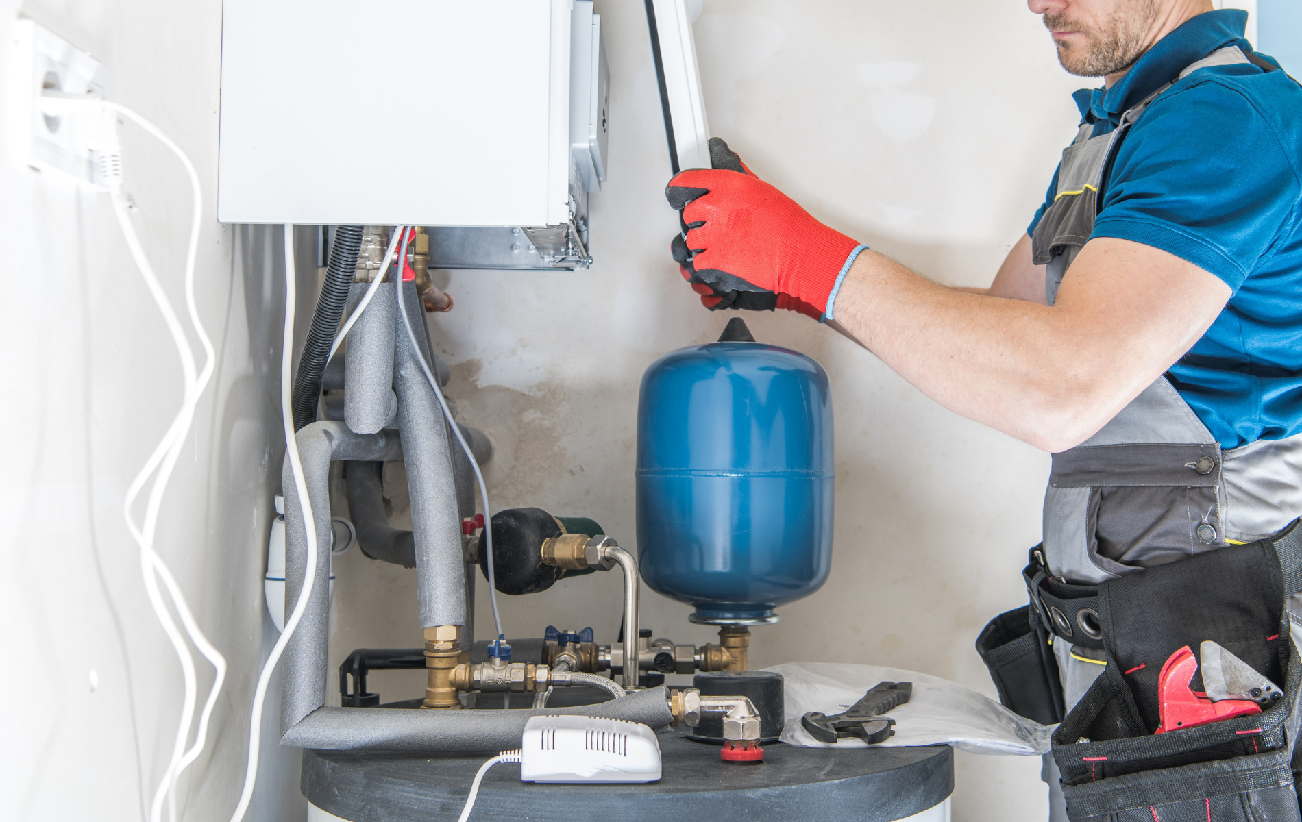 Technician in red gloves inspecting heating equipment with a blue expansion tank in a utility room