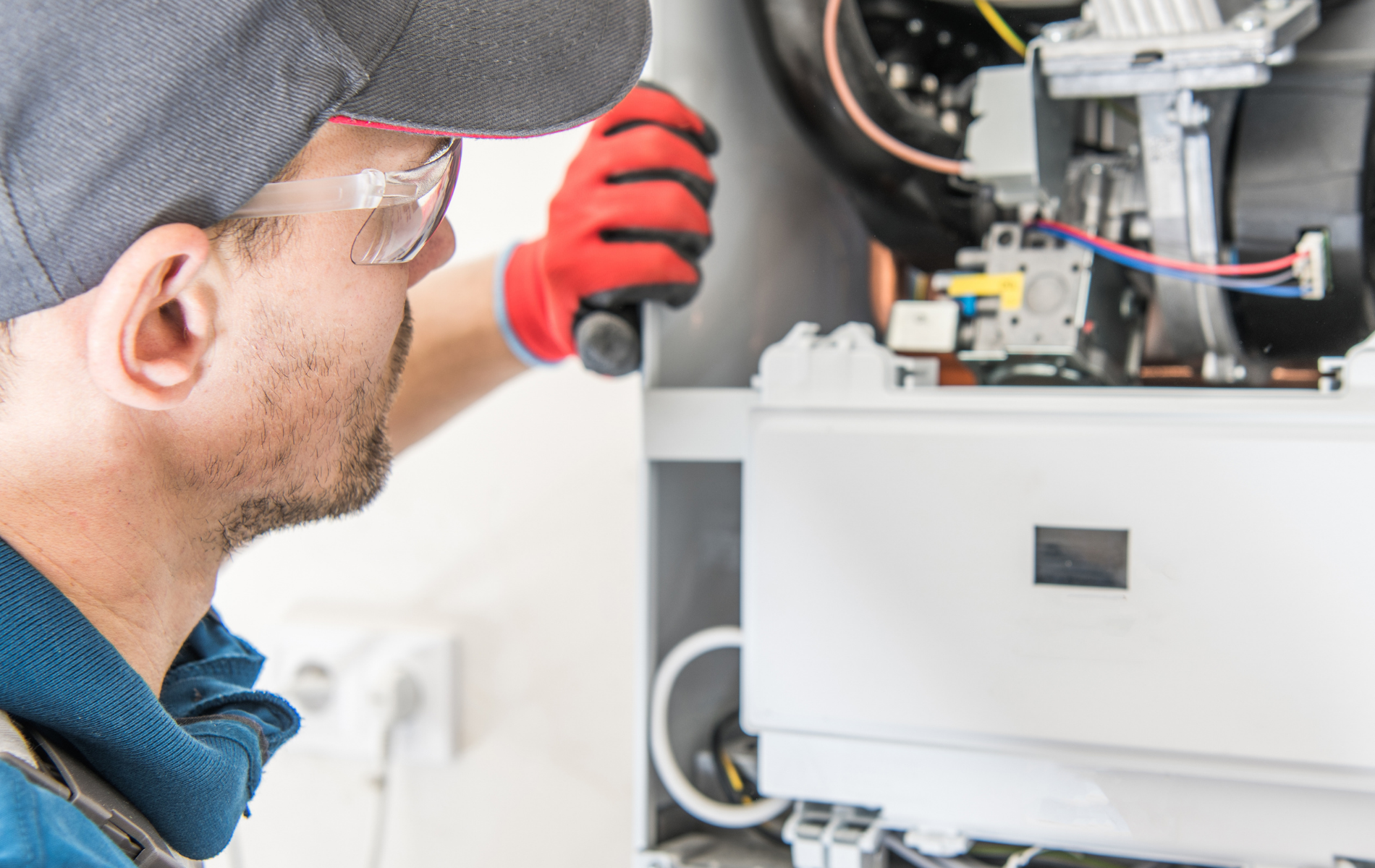 Technician inspecting open appliance wiring with a red glove and cap