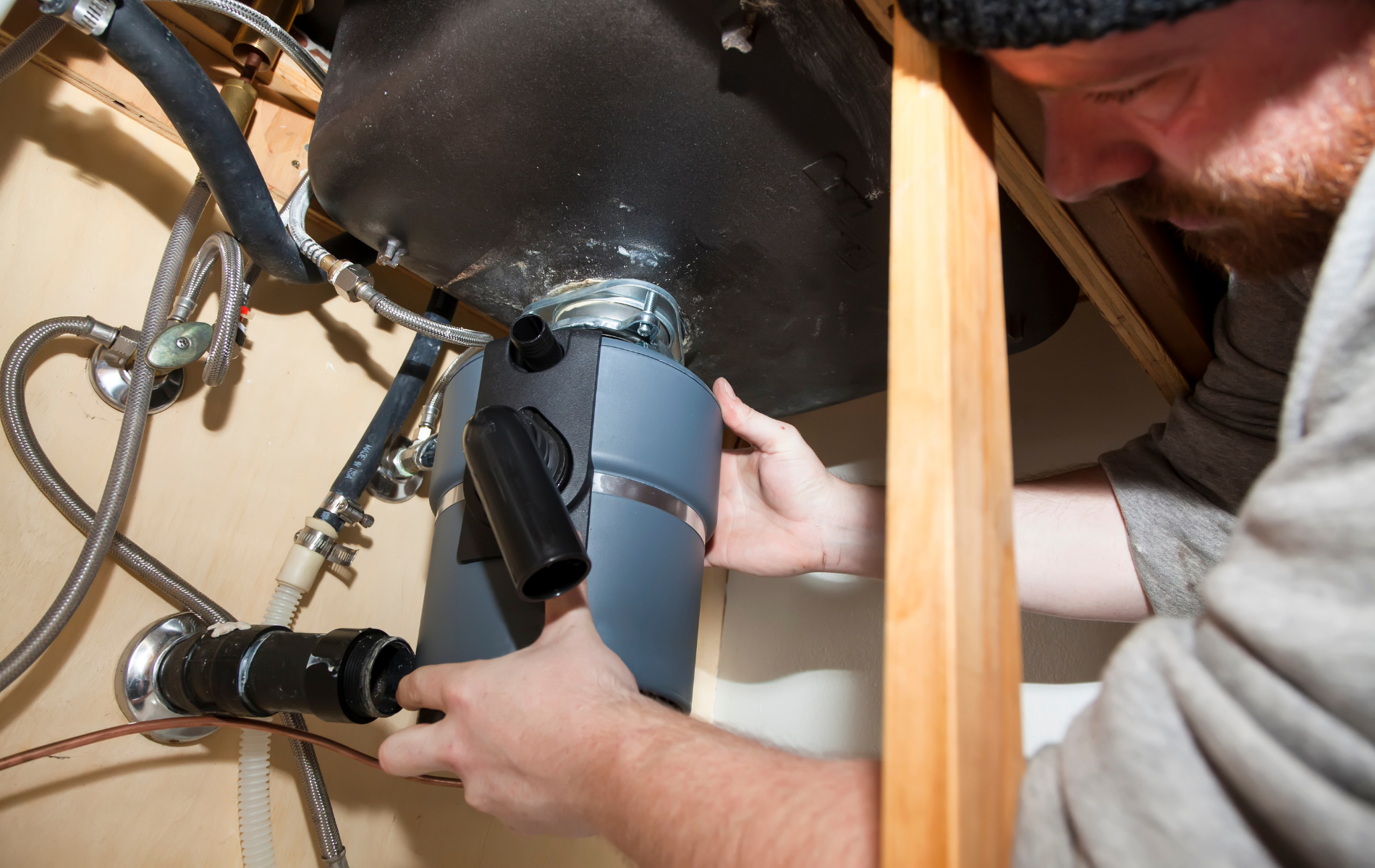 Person installs plumbing under a sink with a wrench and gray drain pipe