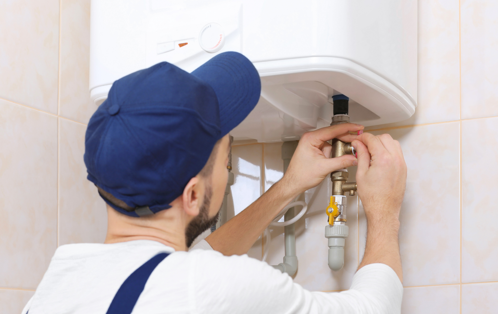 Technician adjusting a wall-mounted water heater with tools in a bathroom cabinet area