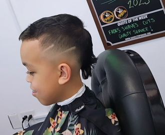 Child with a slicked-back haircut sitting in a barber chair, side profile, looking forward.