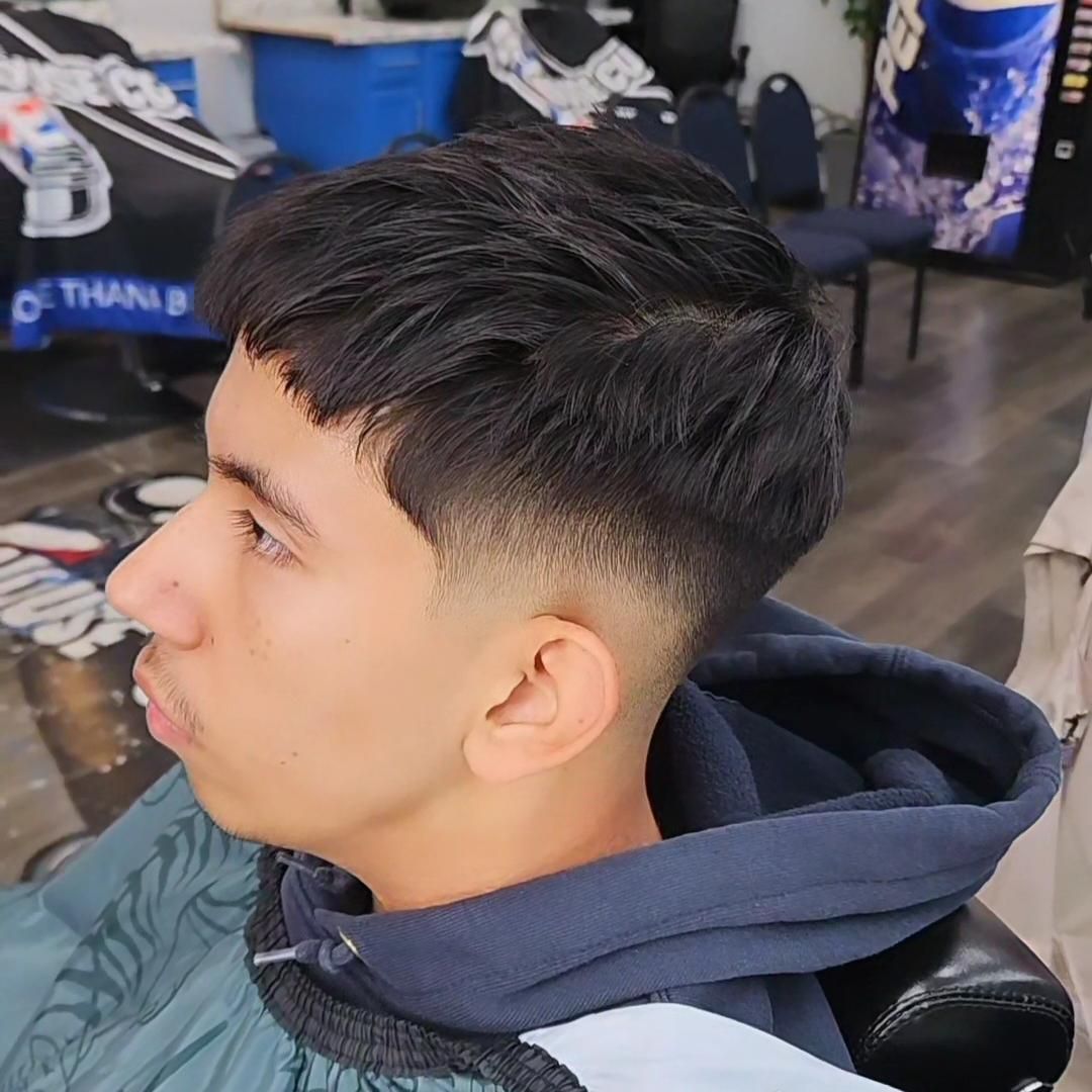 Side-profile haircut with a clean fade and textured dark top in a barbershop chair