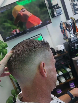 Man with a short fade haircut sitting in a barbershop, seen from behind, with a TV and clippers in the background