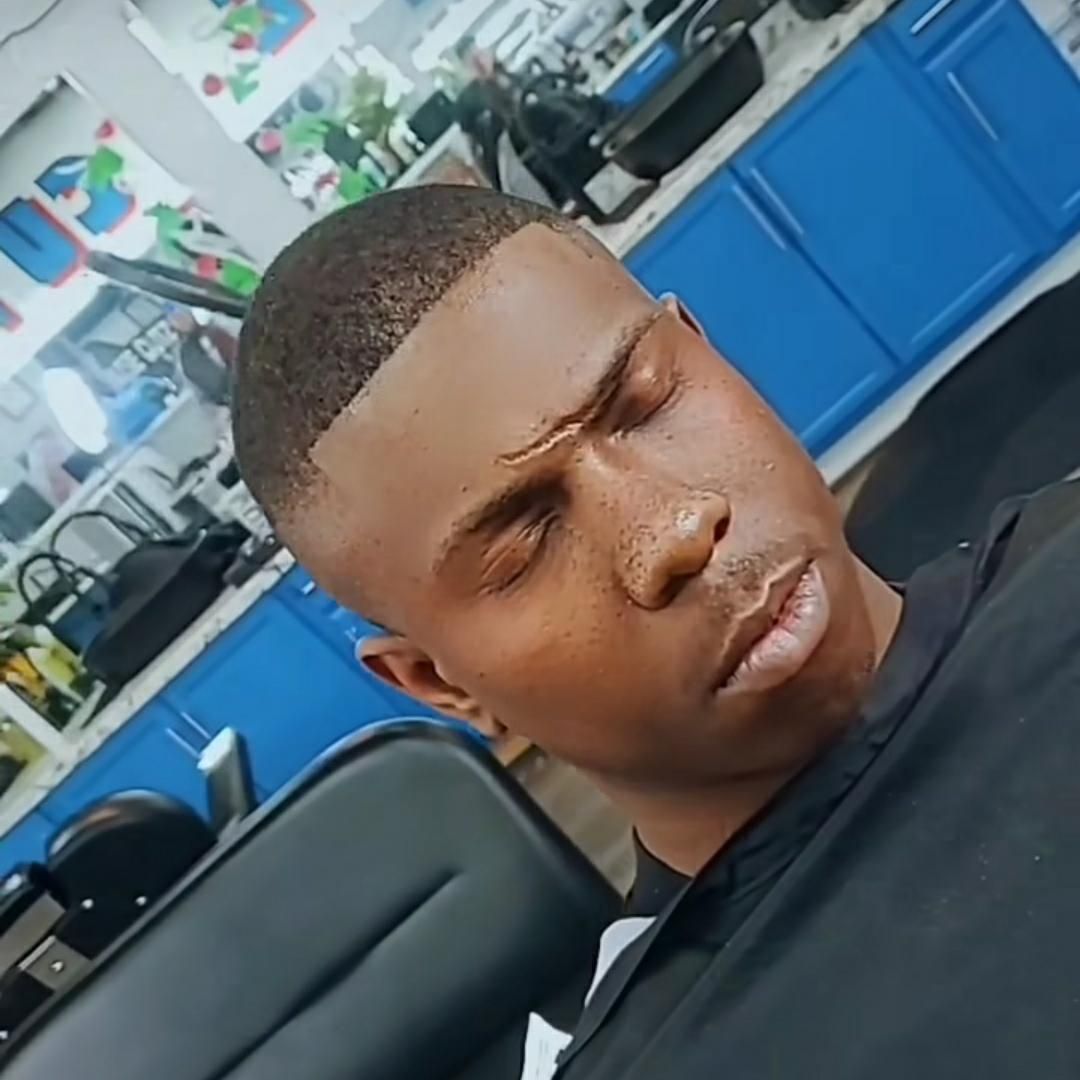 Man with a short haircut sitting in a blue salon chair, looking down with a furrowed brow.