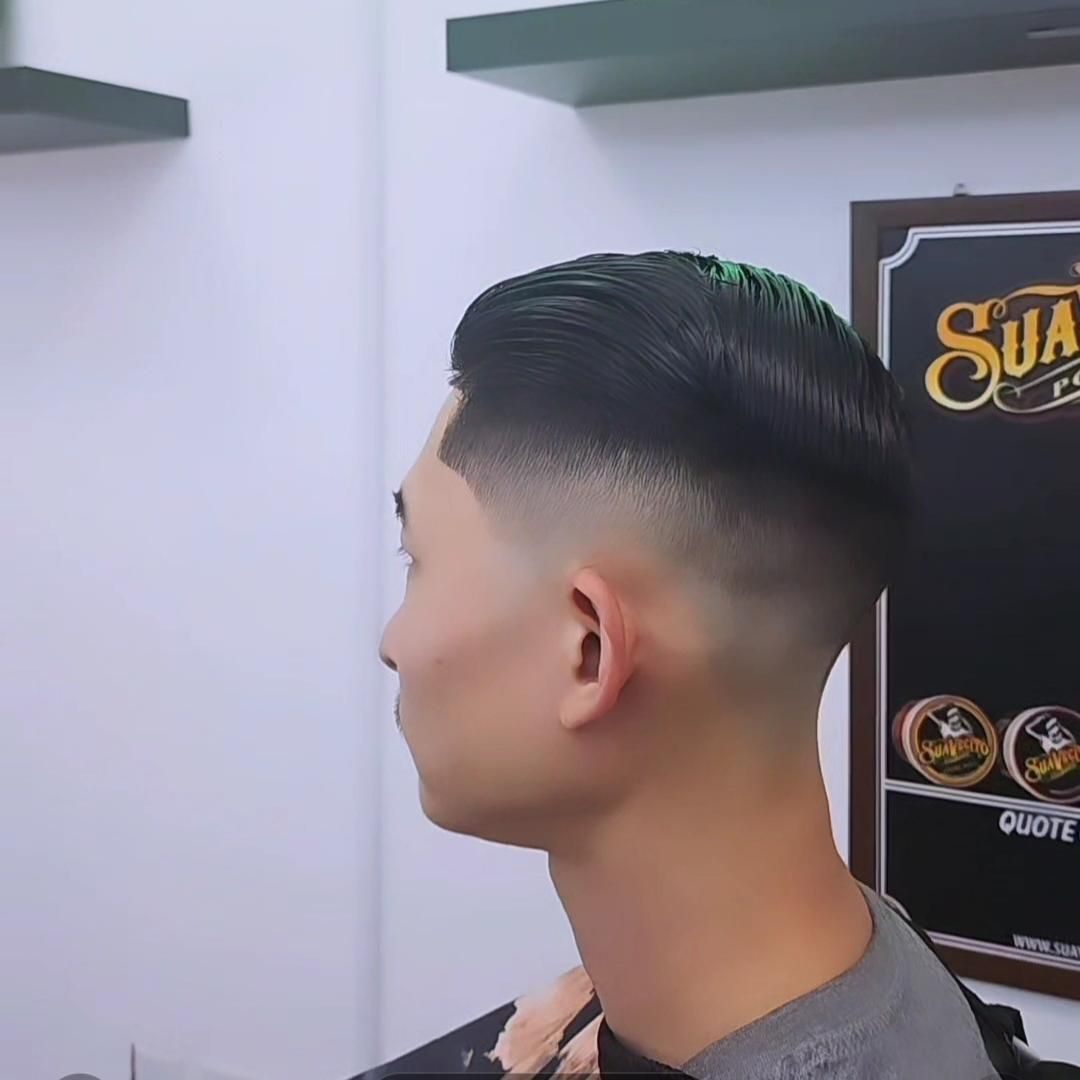 Side profile of a man with a slicked-back fade haircut in a barber shop.