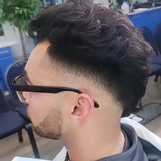 Side profile of a man with a fade haircut and black glasses, seated outdoors.