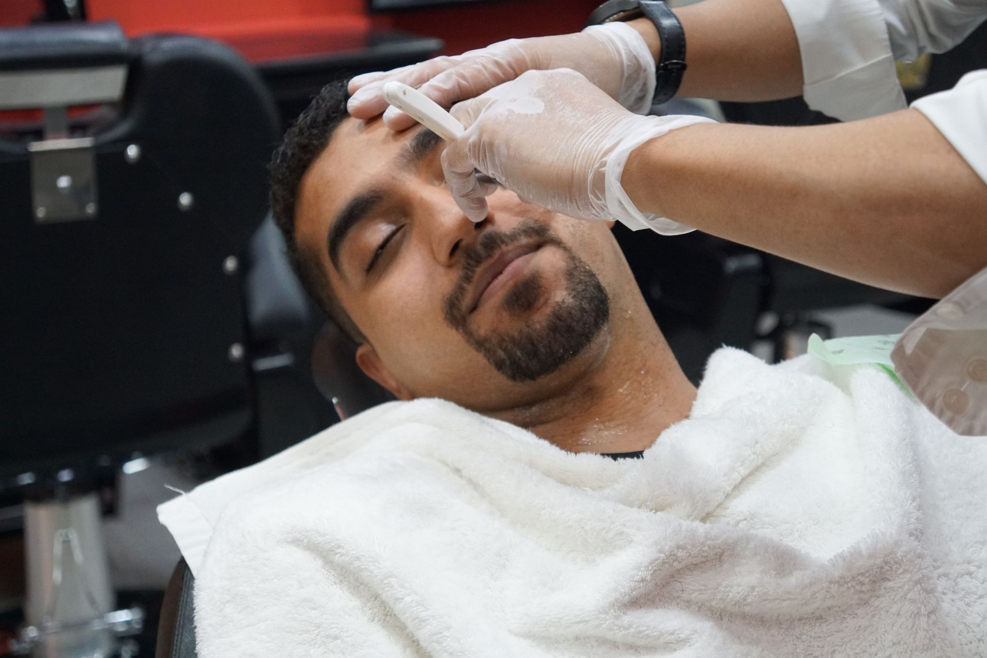 Man reclining in a barber chair while a stylist applies shaving cream to his face