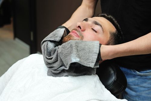 Barber shaving a man’s beard with a straight razor and towel around his neck