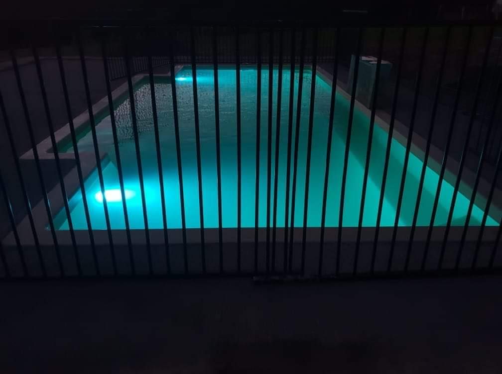 Glowing Blue Pool Behind a Black Metal Fence at Night — Clearwater Pools Hallidays Point in Harrington, NSW
