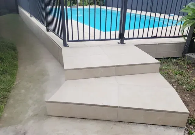 Pool steps with beige tile leading up to a fenced swimming pool.
