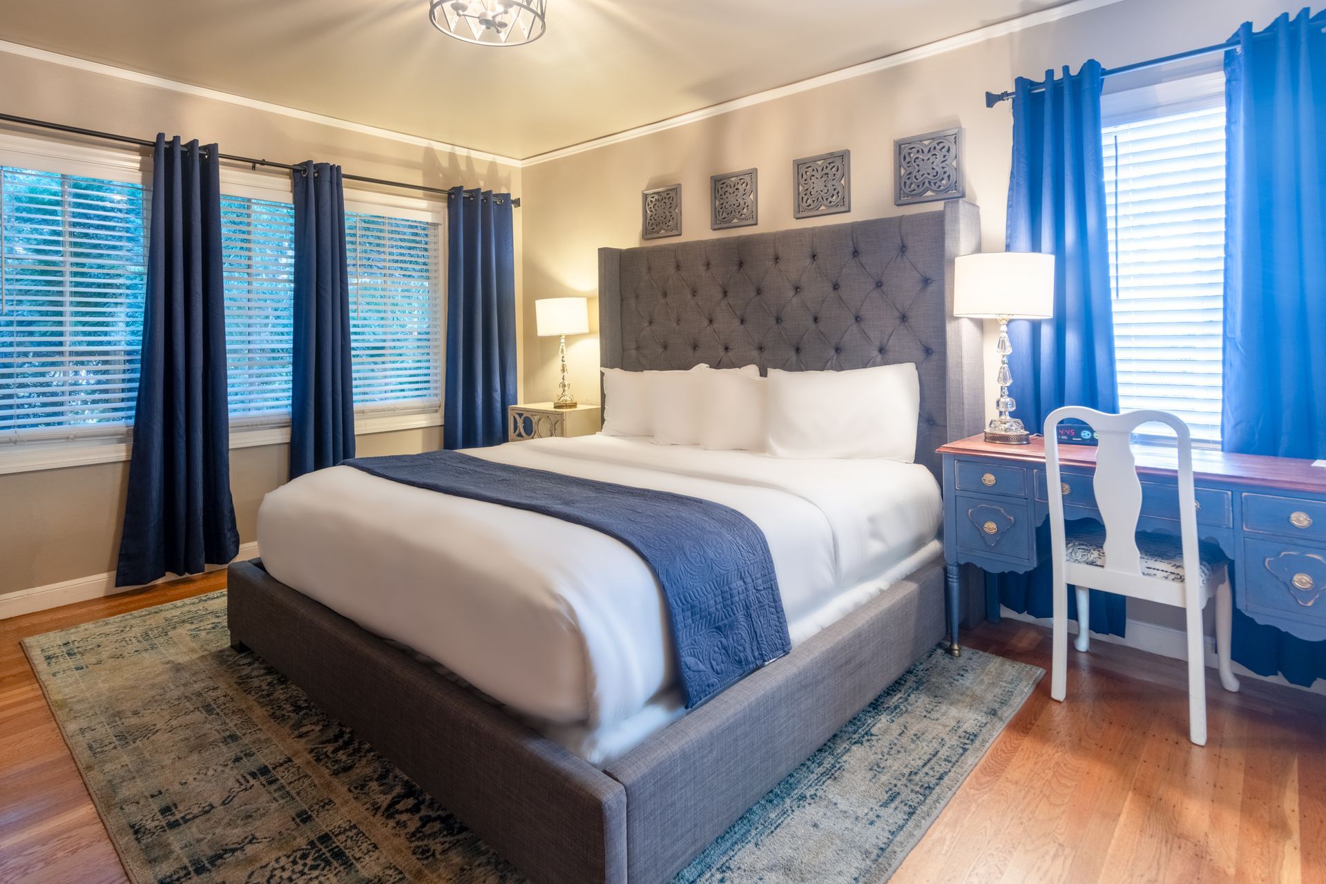 A bedroom with a king size bed , desk , chair and blue curtains.