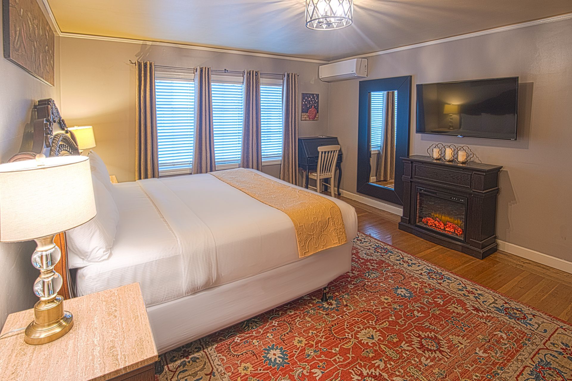 A bedroom with a king size bed , fireplace , television and a rug.