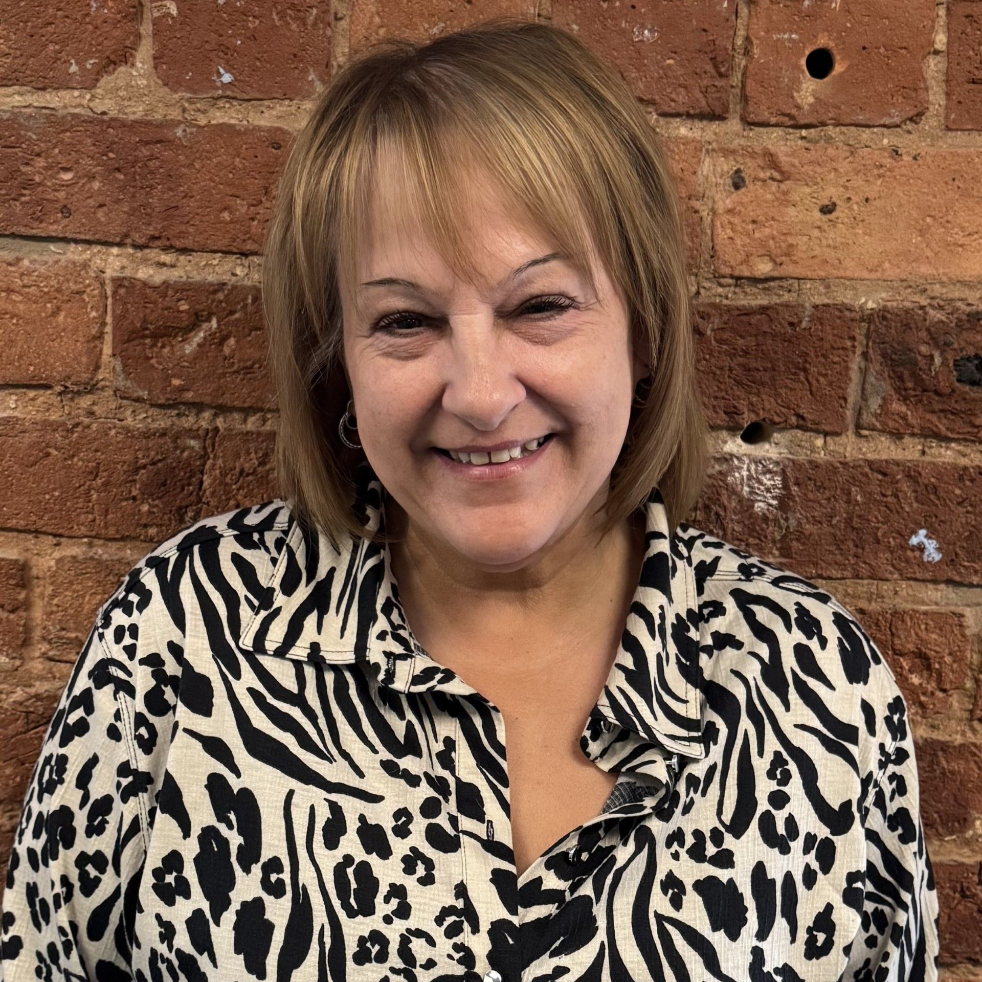 A woman wearing a black shirt and a heart necklace is smiling for the camera.