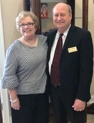 Woman in patterned top and man in suit stand together.