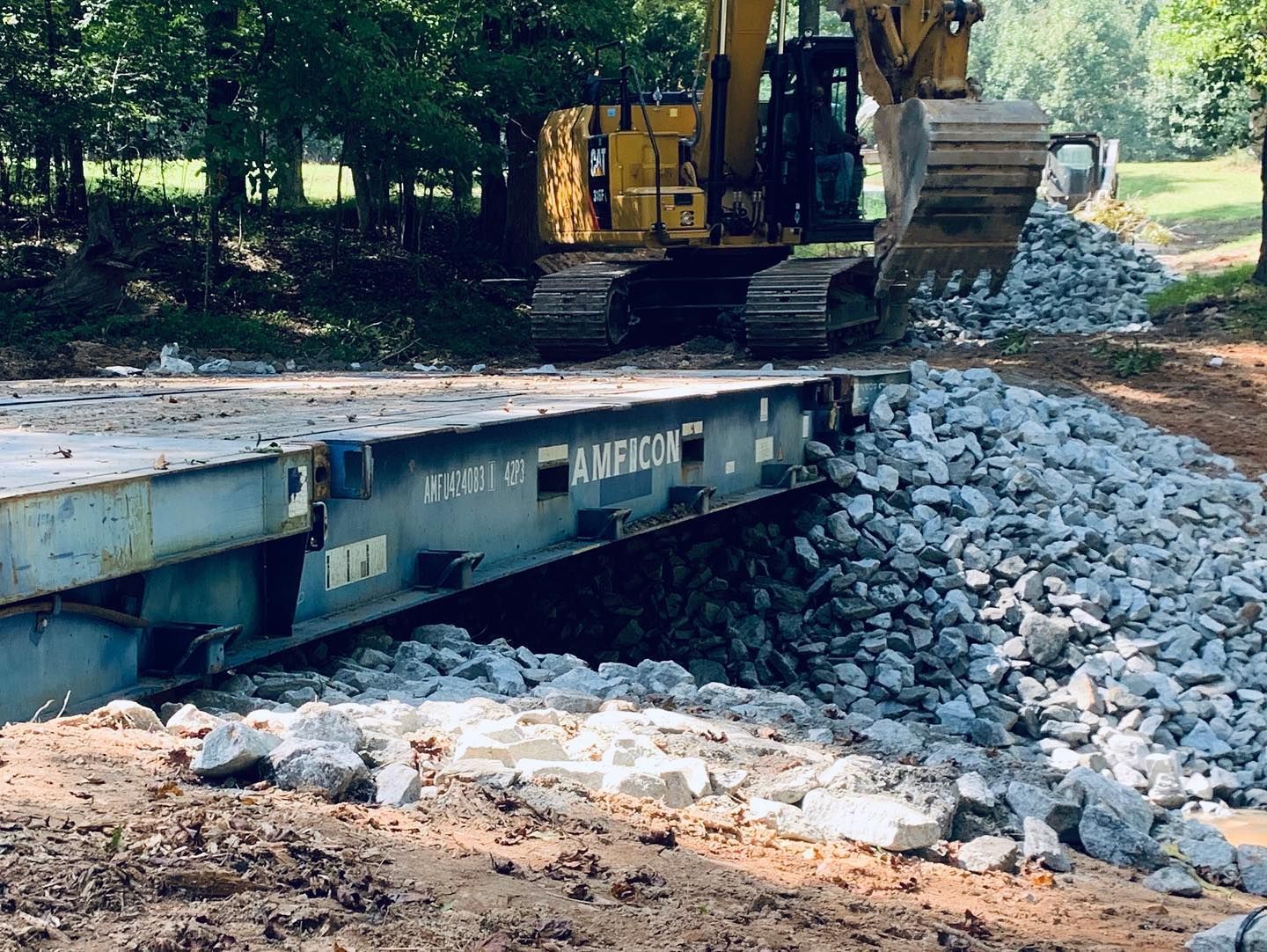 A yellow excavator places rocks to build up the sides of a container bridge.