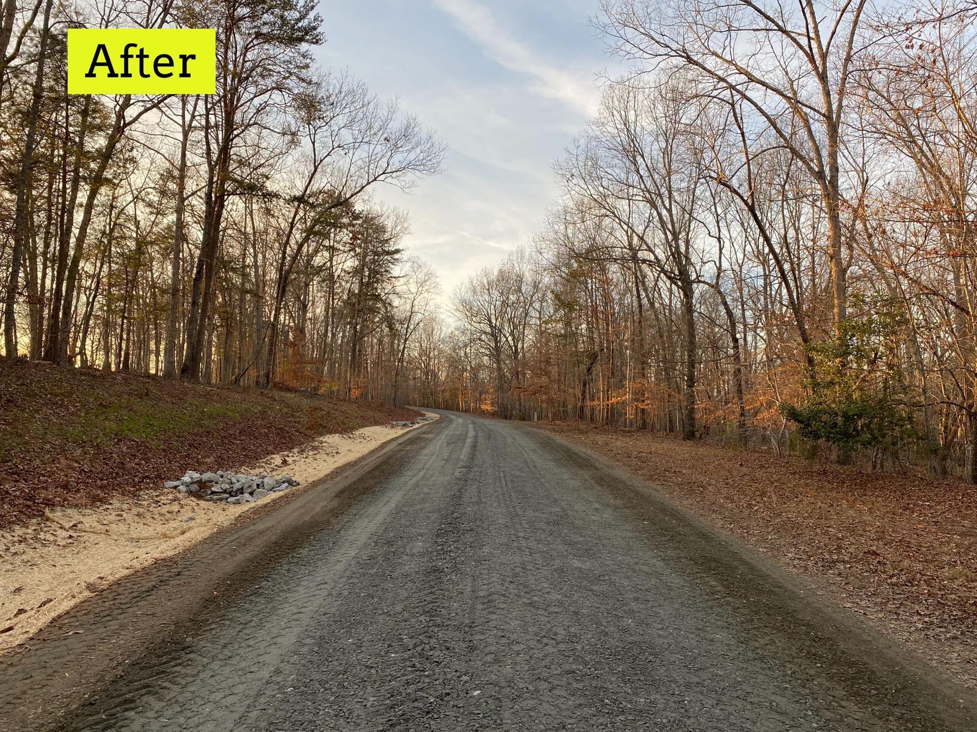 Gravel road through a forest; trees line both sides with autumn foliage; cloudy sky in the distance.