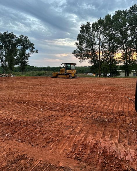A yellow bulldozer on a dirt lot, evening sky with trees in the background.