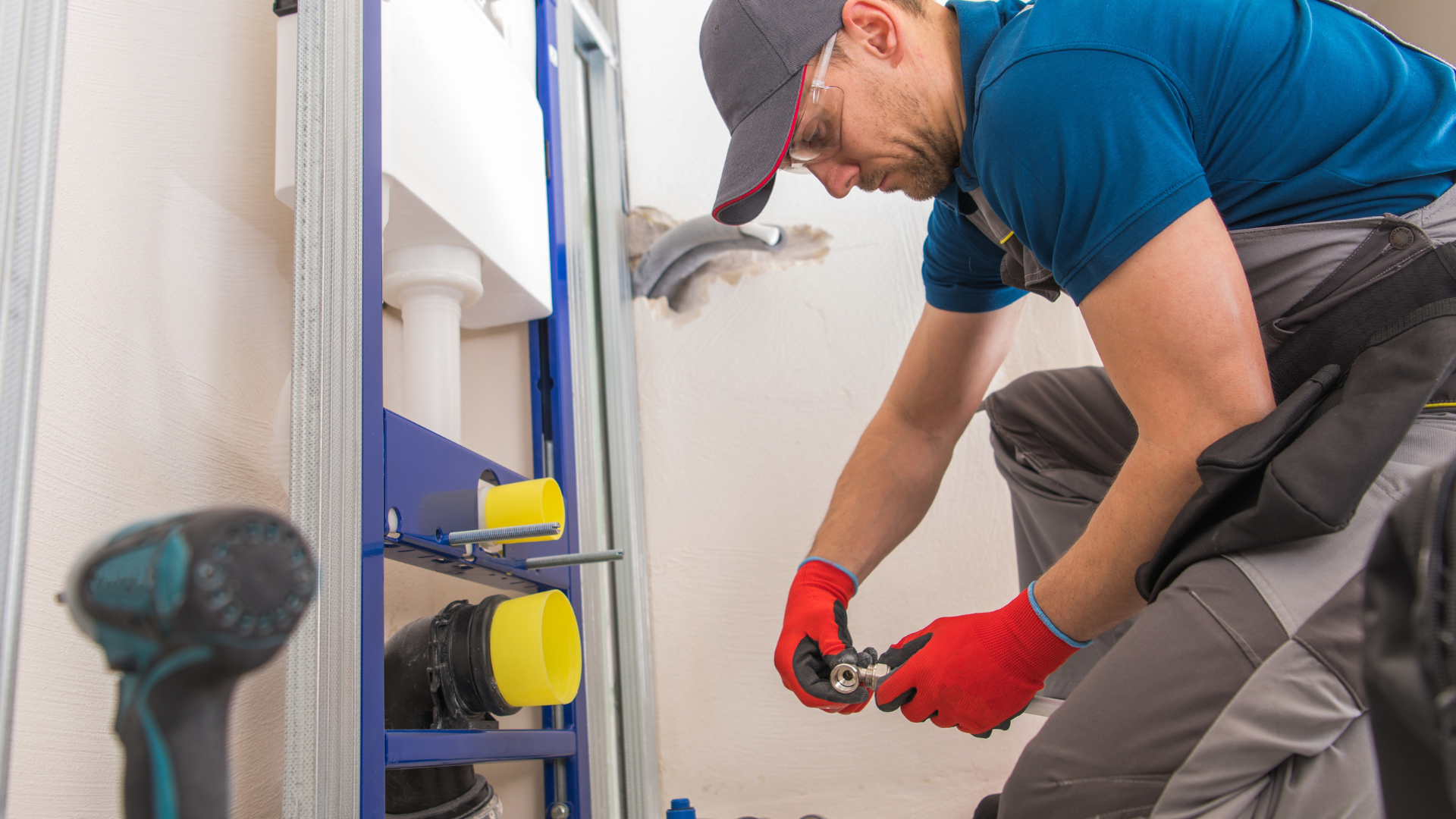 Plumber in red gloves tightening a pipe under a sink in a bathroom cabinet