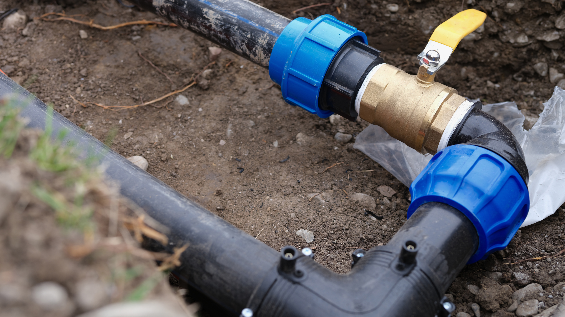 Black pipes with blue connectors and a brass valve in a trench.