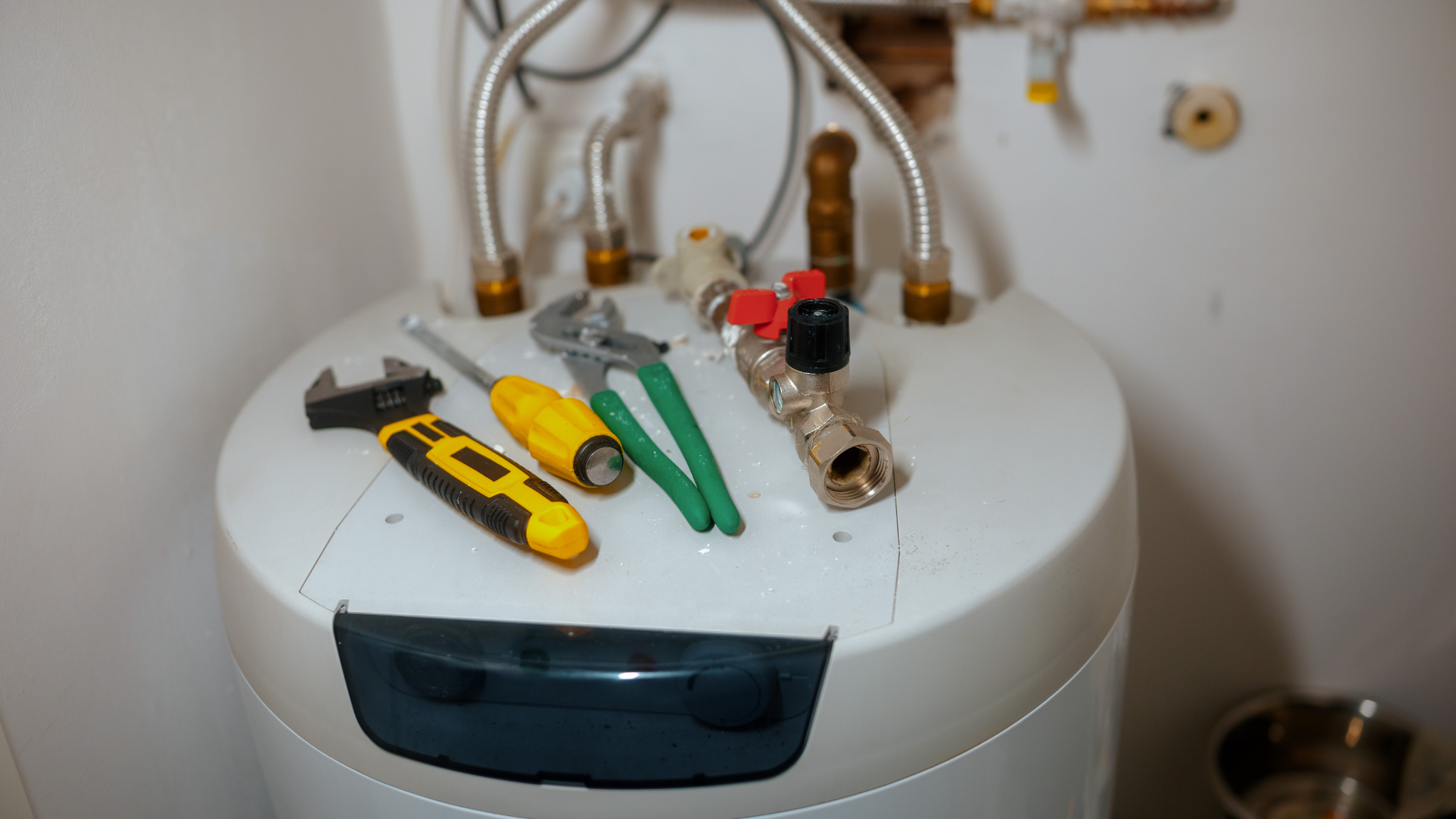 Tools atop a white water heater, including a wrench, screwdriver, pliers, and valve.