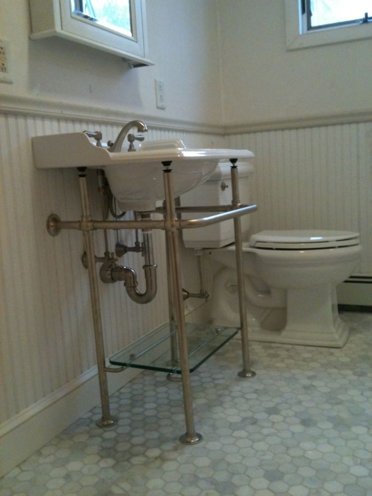 Bathroom with a pedestal sink, toilet, and hexagonal tile floor. Beadboard walls.